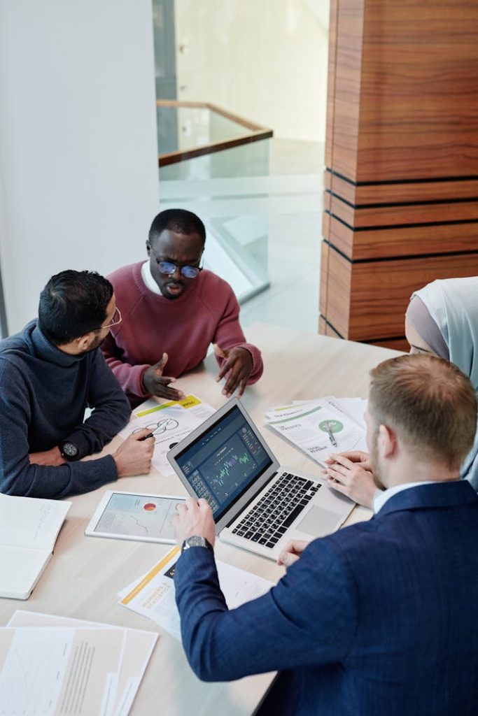 A diverse group of professionals collaborating in an office setting with laptops and documents.